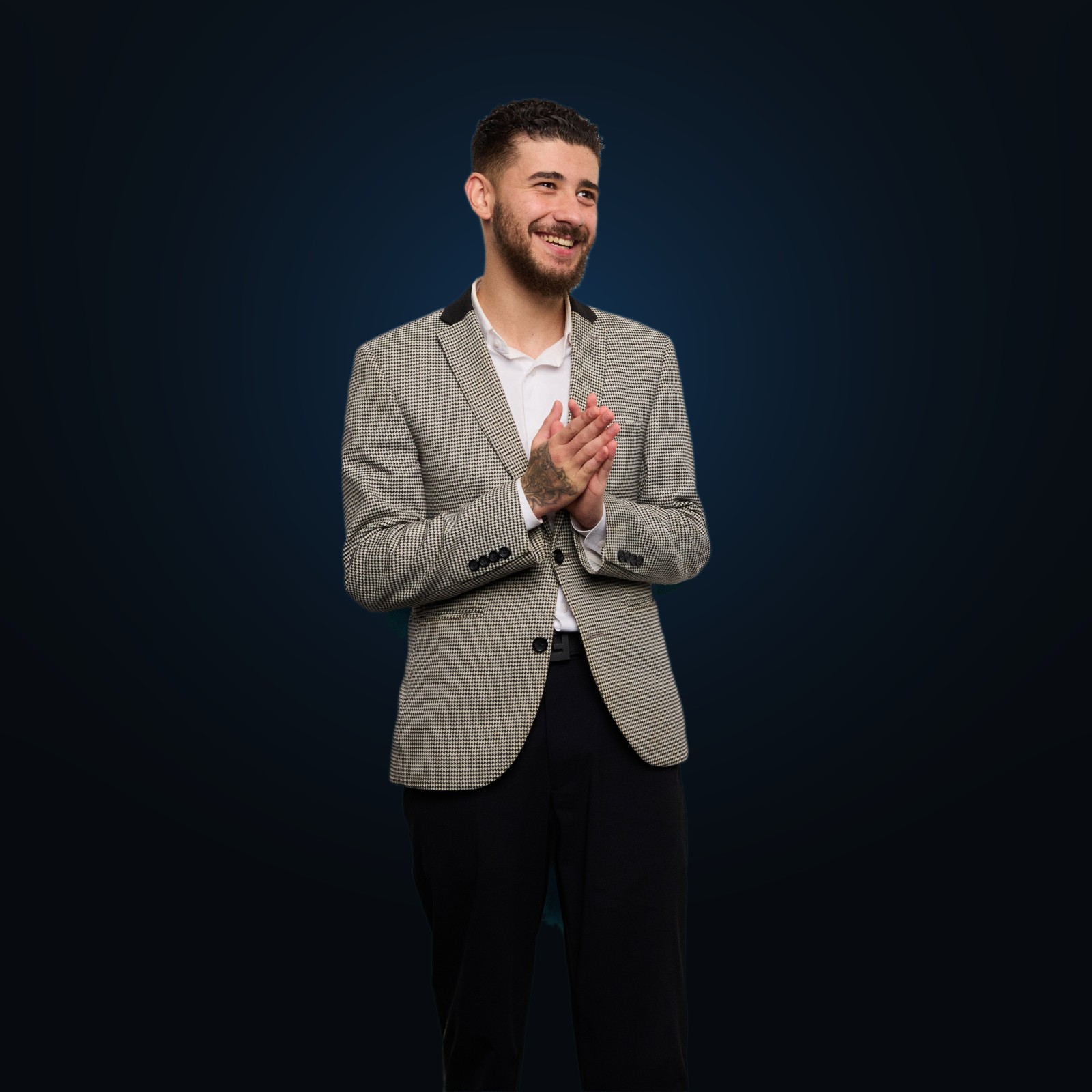 Brodie Macklin, founder of VVS Digital Solutions, smiling in a houndstooth blazer against a deep blue-lit studio backdrop
